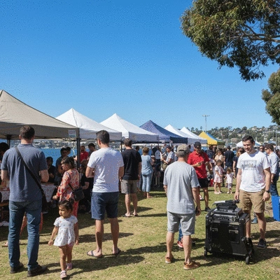 Diverse group of people enjoying a vibrant community festival in Mordialloc, with food stalls, live music, and children playing